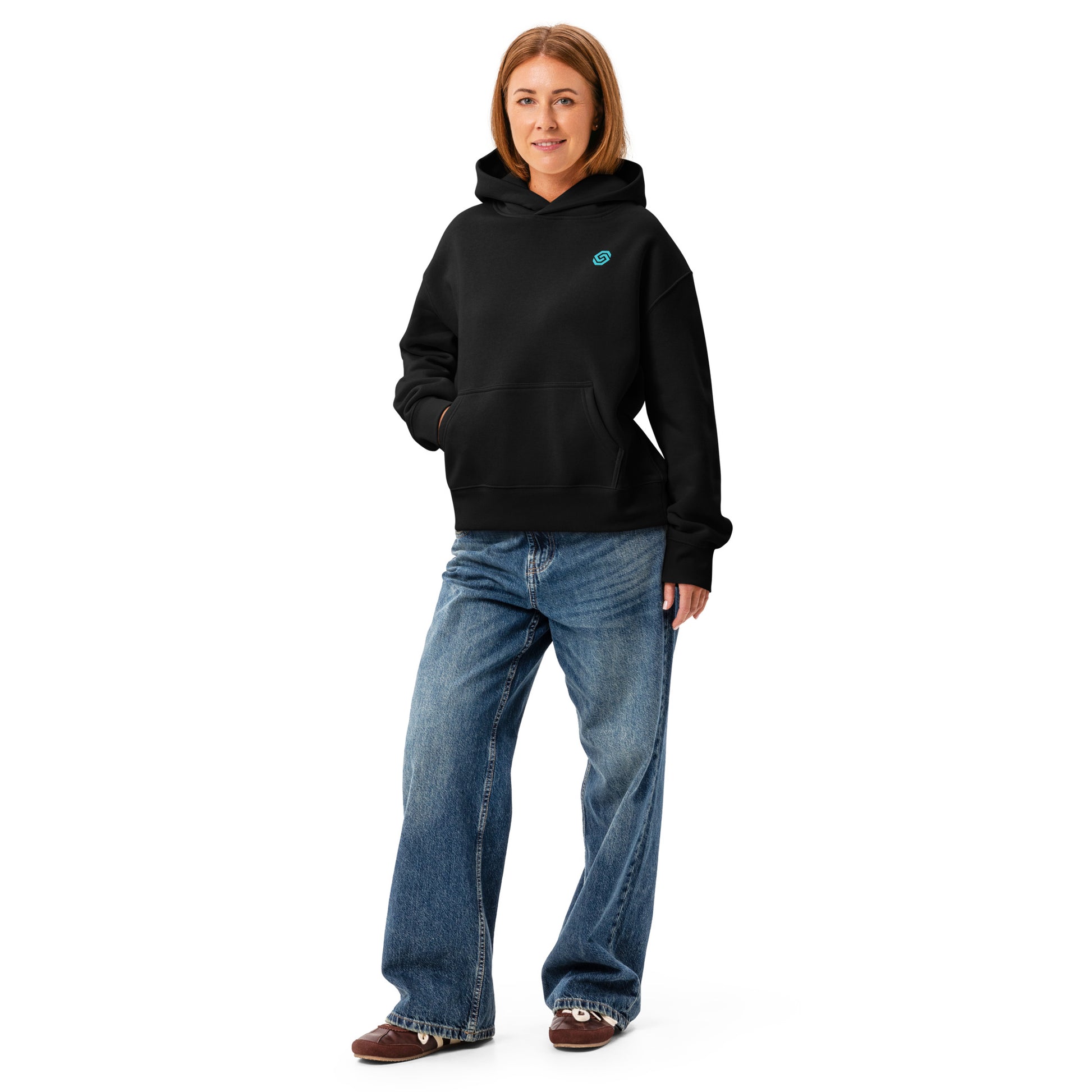 A woman standing with hand in pocket wearing a HUDL women's relaxed fit pullover hoodie – off-court squash style, embroidered logo in black