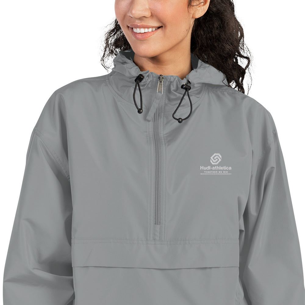 A close up of a woman wearing the HUDL lightweight packable windbreaker jacket – squash warm-up gear, embroidered logo in grey