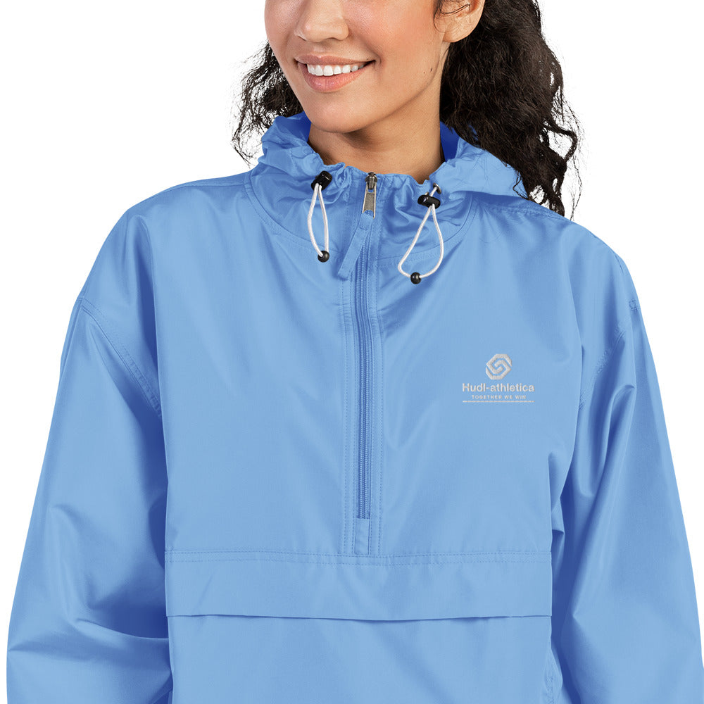 A close up woman wearing the HUDL lightweight packable windbreaker jacket – squash warm-up gear, embroidered logo in light blue