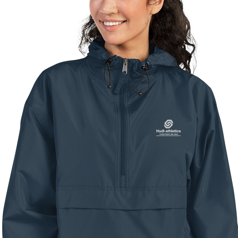 A close up of a woman wearing the HUDL lightweight packable windbreaker jacket – squash warm-up gear, embroidered logo in navy