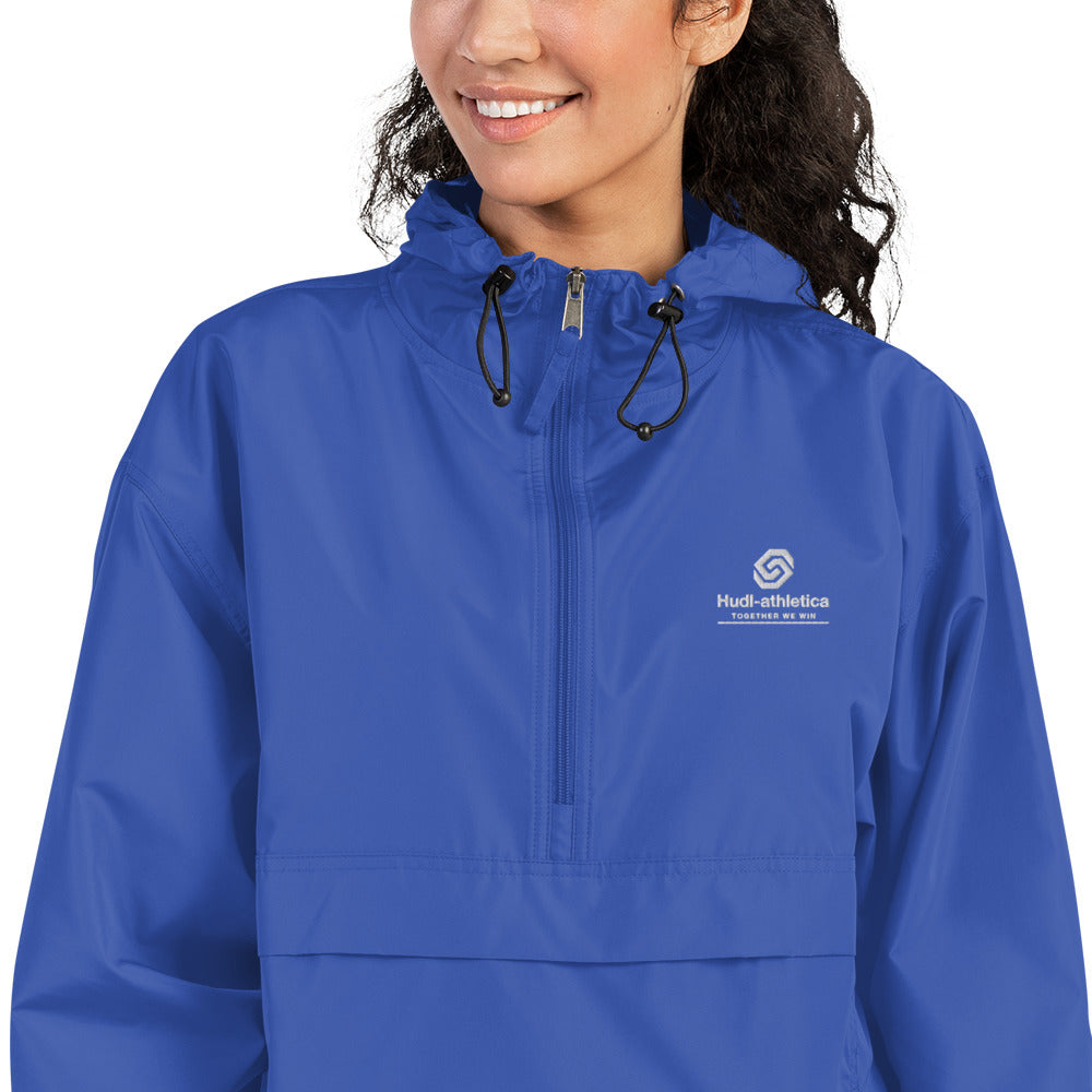 A close up of a woman wearing the HUDL lightweight packable windbreaker jacket – squash warm-up gear, embroidered logo in royal 