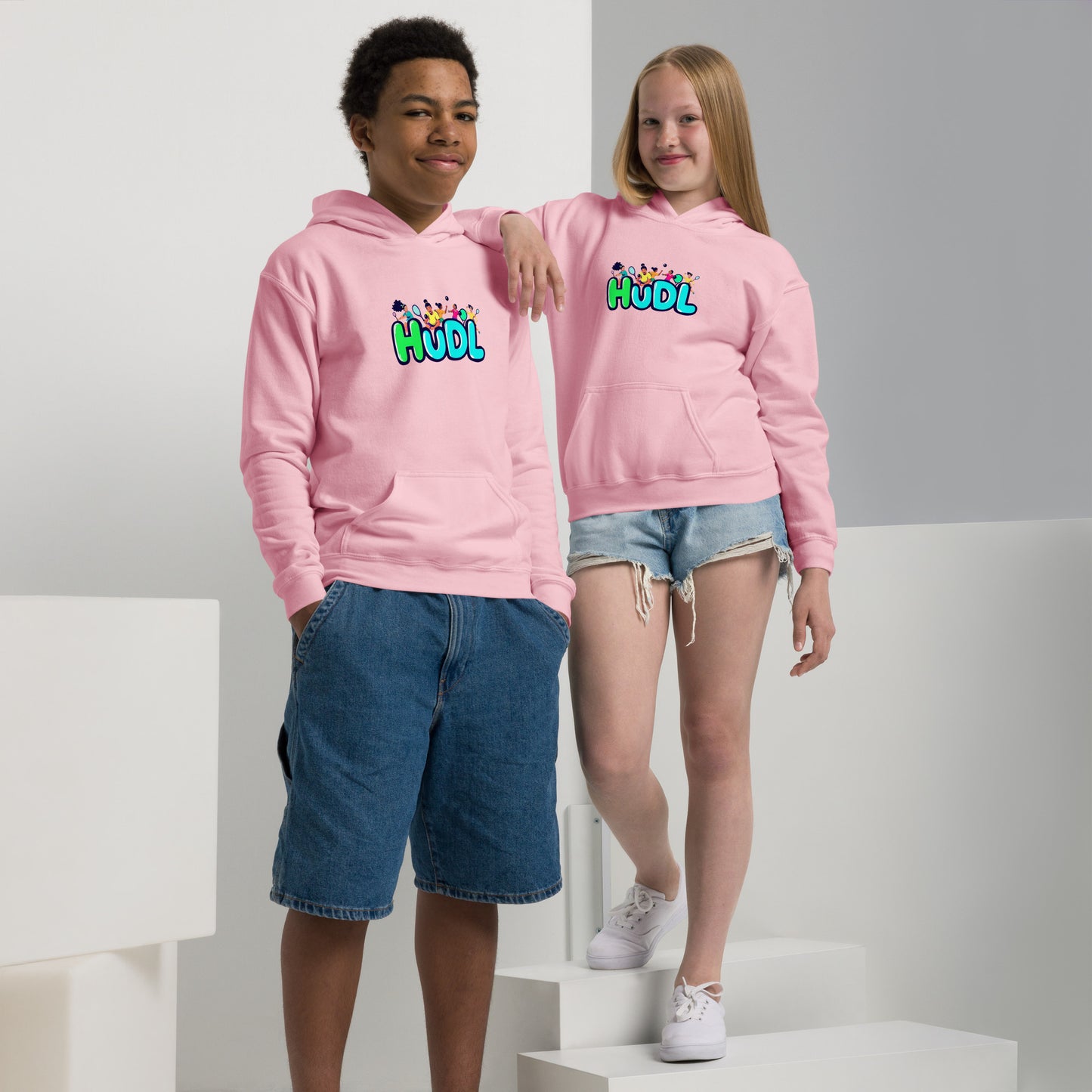 A boy and a girl standing and wearing a HUDL youth heavy blend hoodie – warm, durable off-court hoodie for junior squash players in pink